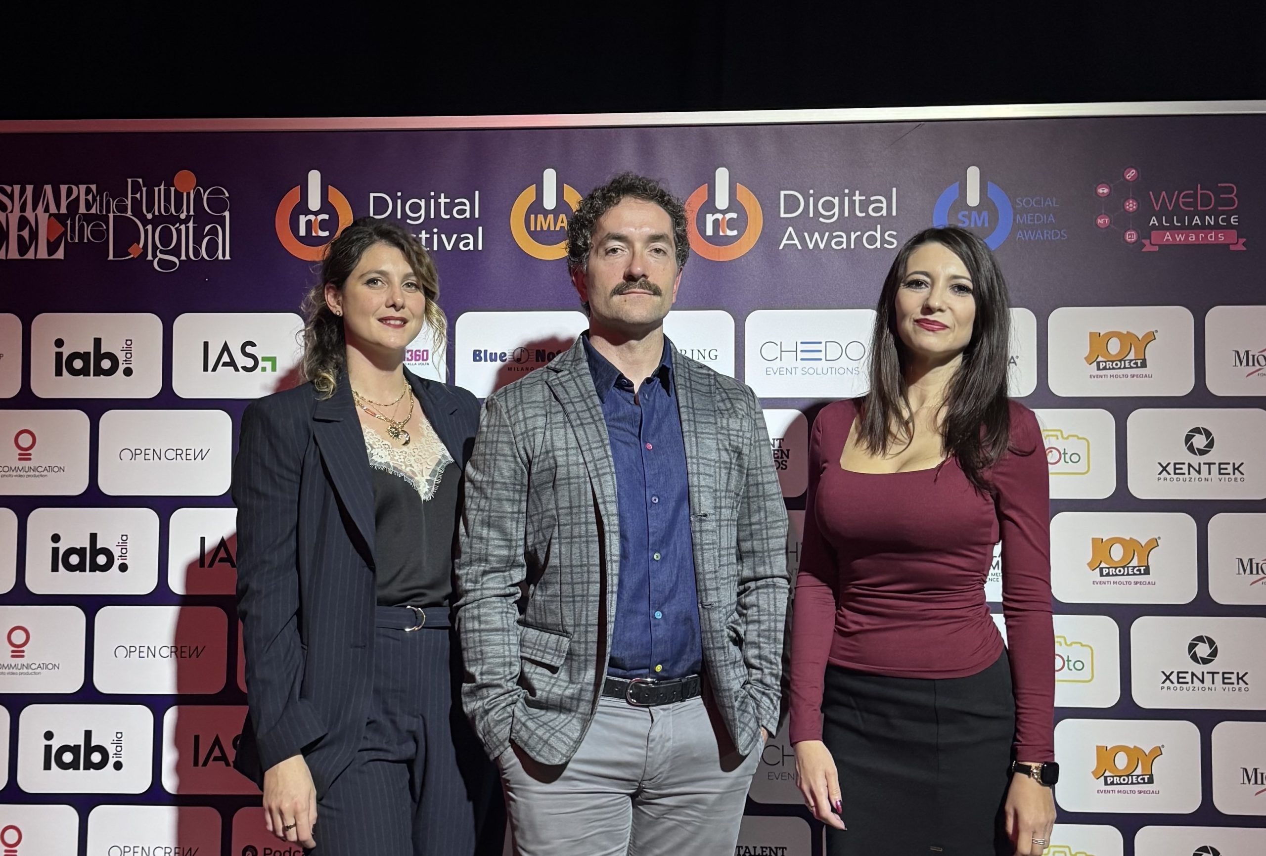 Kleecks_for_Web3 Three Kleecks team members posing in front of a digital awards event backdrop filled with sponsor logos. Two women and one man are dressed in formal business attire and smiling for the photo.